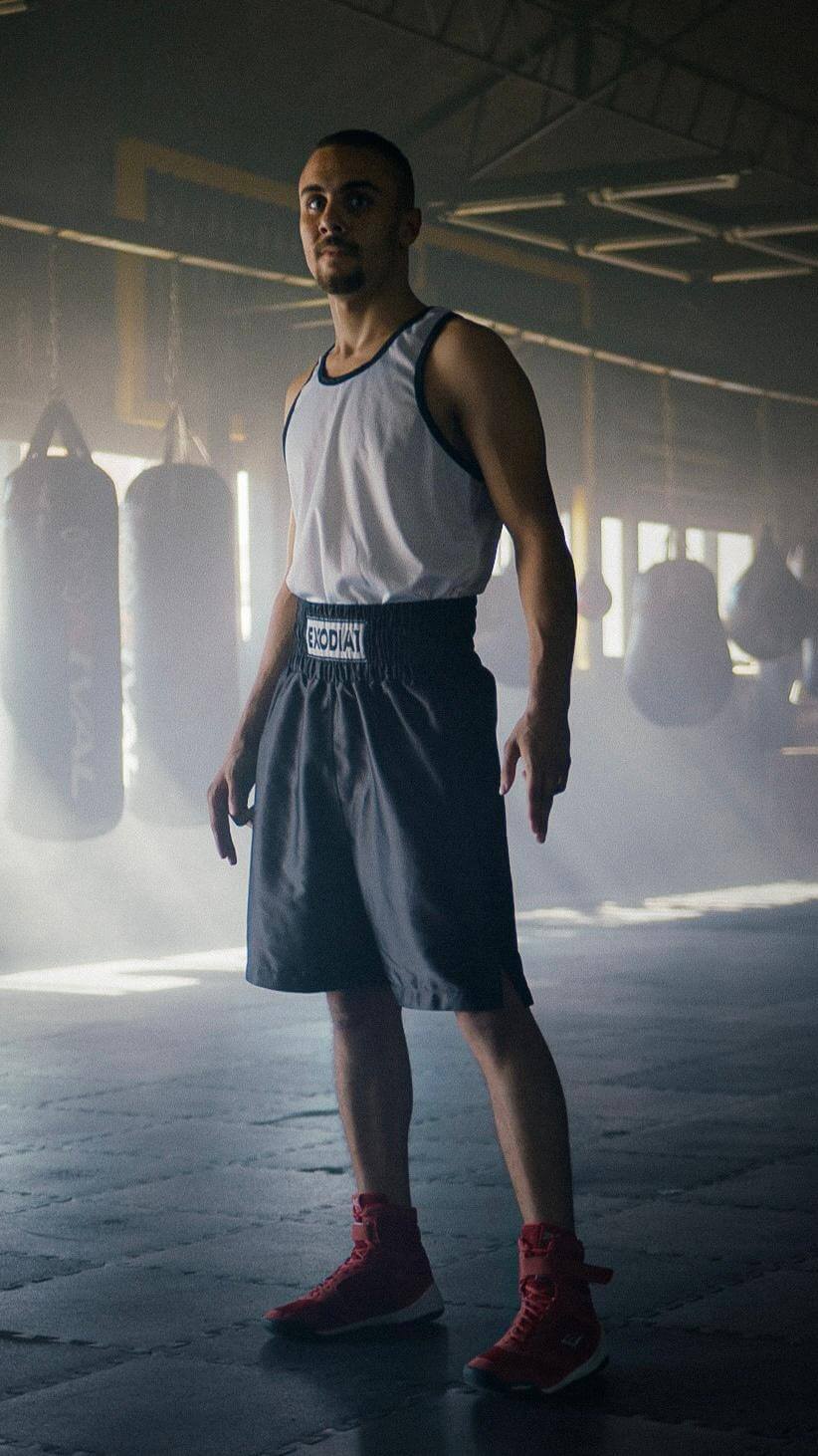 Man wearing Exodia 1 Sports satin boxing shorts in black standing in a boxing gym with punching bags