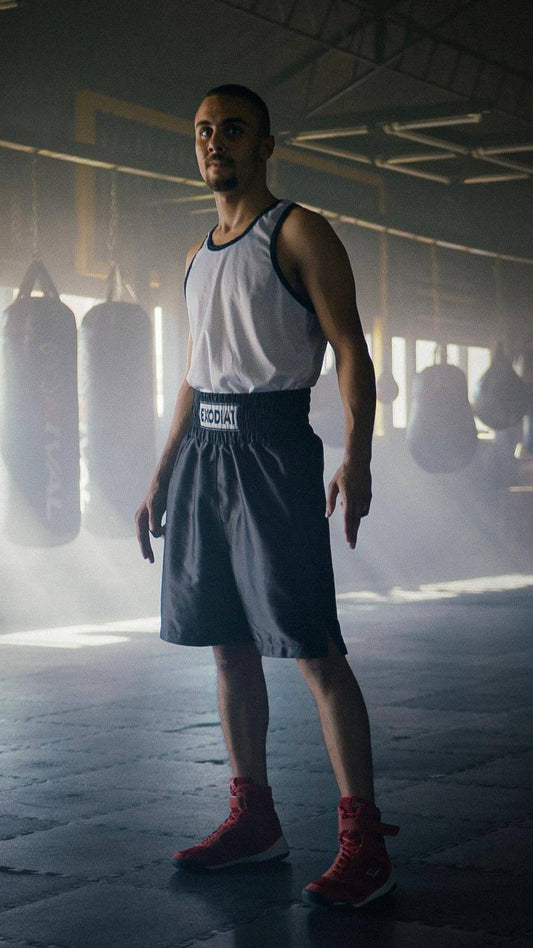 Man wearing Exodia 1 Sports satin boxing shorts in black standing in a boxing gym with punching bags